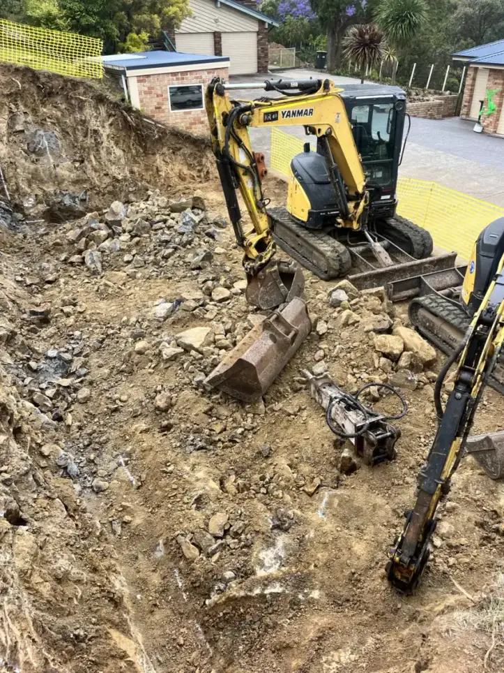 An excavator digging out footings and drainage on a cleared suburban block.
