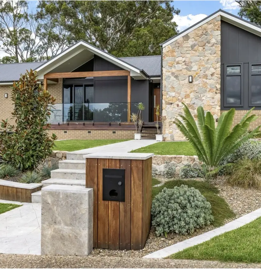 A stone-and-render house frontage with a timber-clad pier letterbox and native front garden.