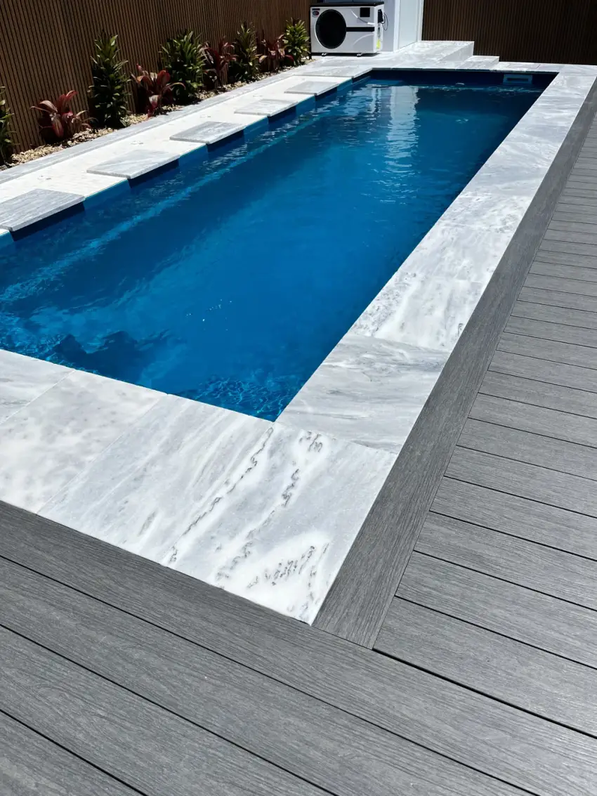 A deep-blue tiled lap pool with a travertine surround and composite timber decking.