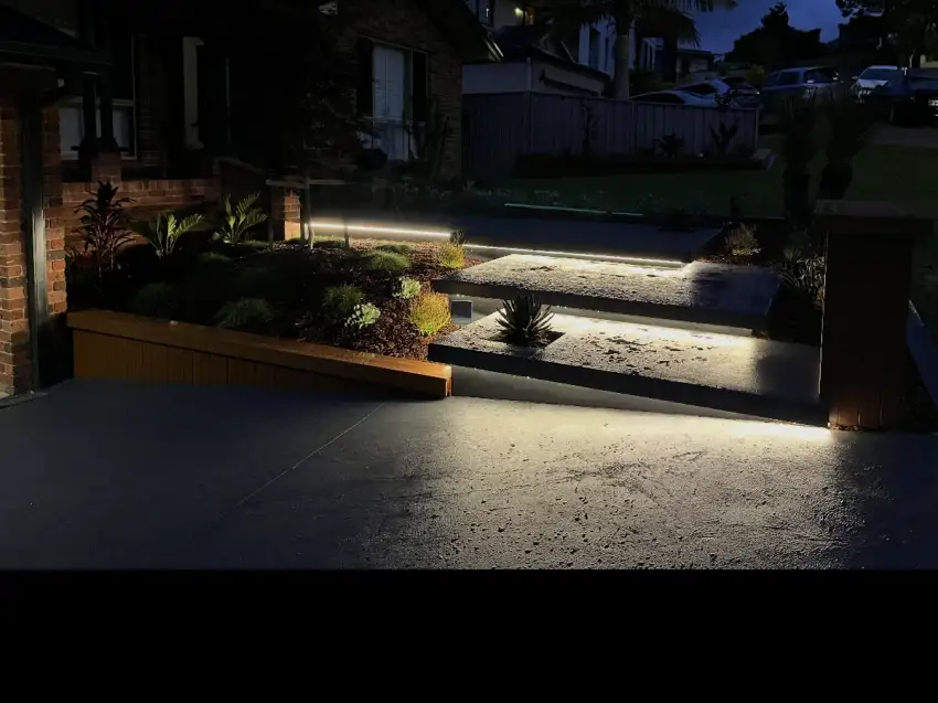 A paved driveway and path lit at night by low garden lighting.
