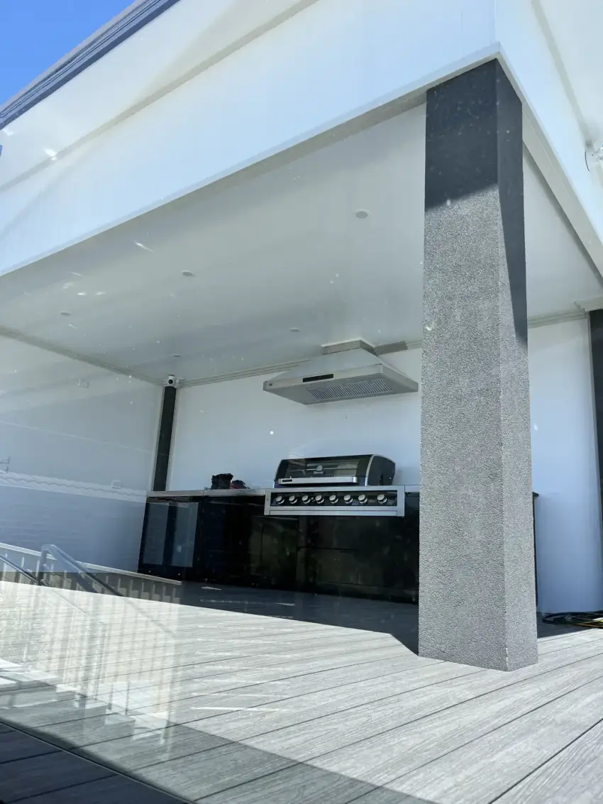 A covered outdoor kitchen with a built-in BBQ and rangehood over composite decking.