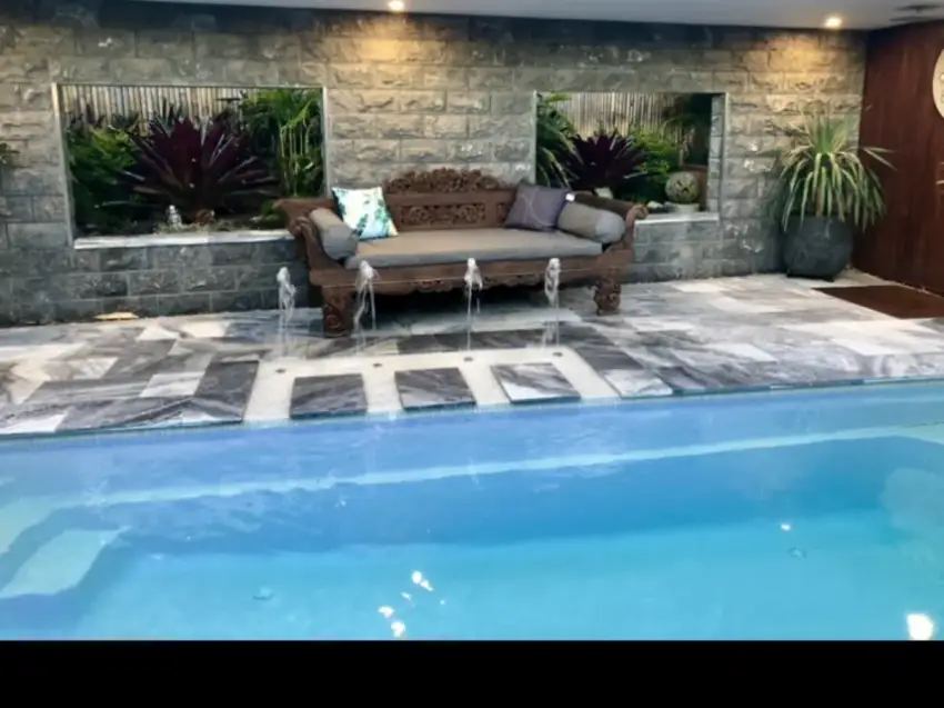 A finished pool with water jets, a carved timber daybed and a stacked-stone feature wall.