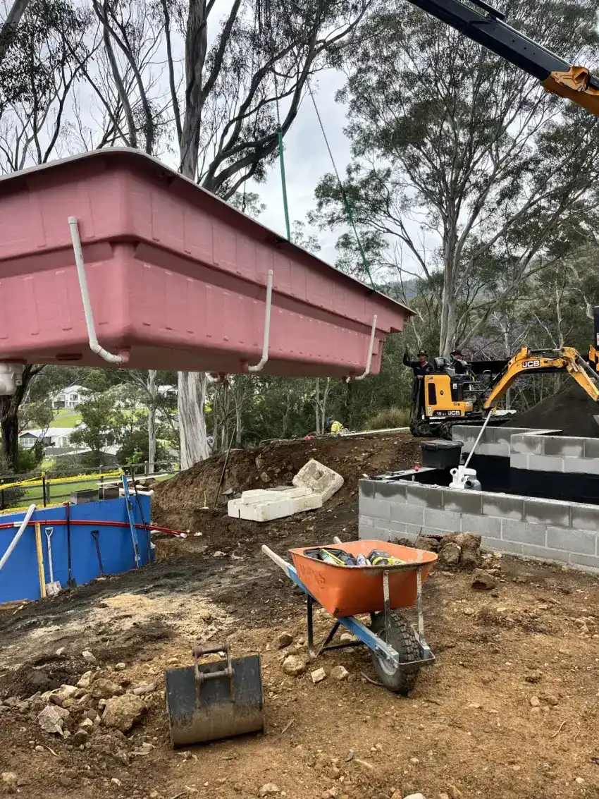An excavator clearing and benching a sloped block, with spoil stockpiled ready to cart out.