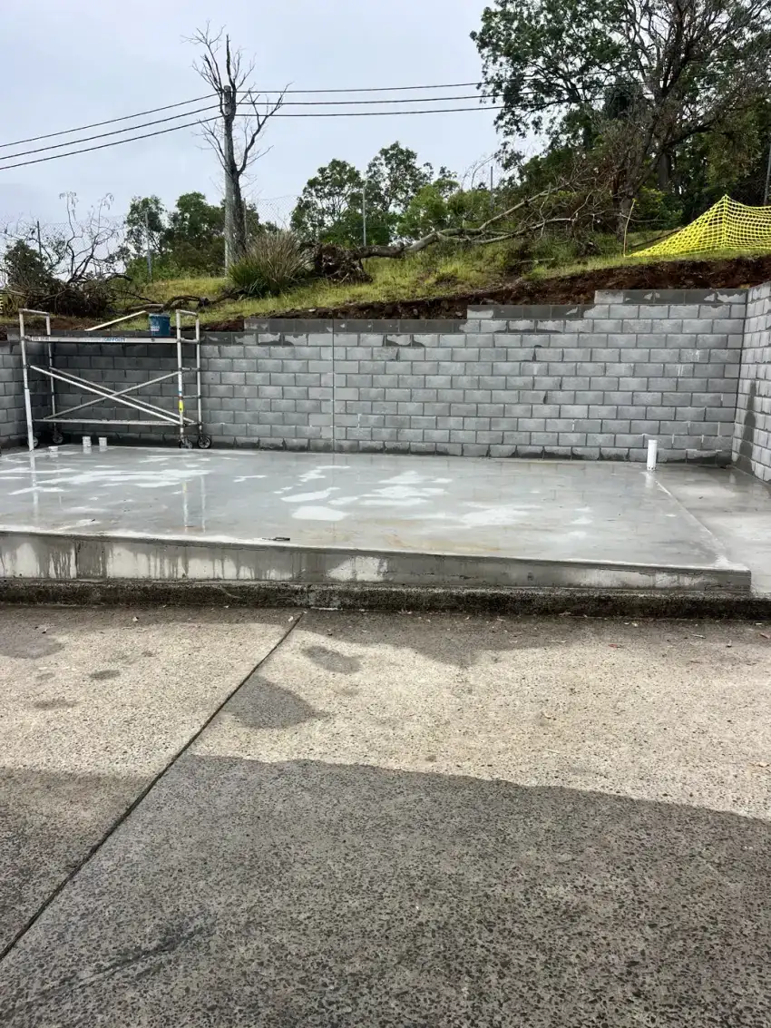 A poured concrete slab beside a rendered block retaining wall on a prepared site.