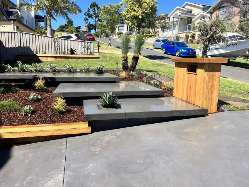 Bluestone stepping stones set through a lawn beside a timber letterbox planter and driveway.