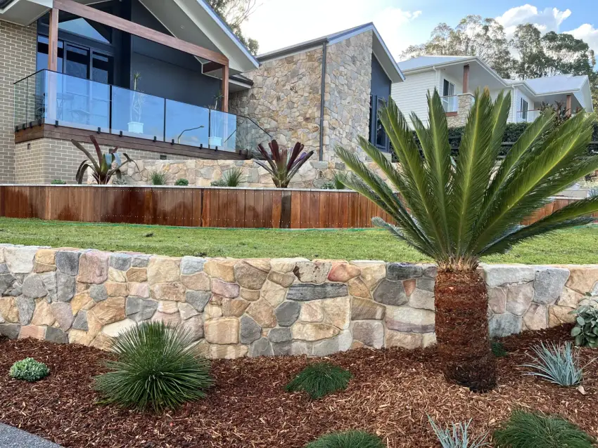 A natural sandstone block retaining wall and planted frontage with a grass tree and mulched beds.