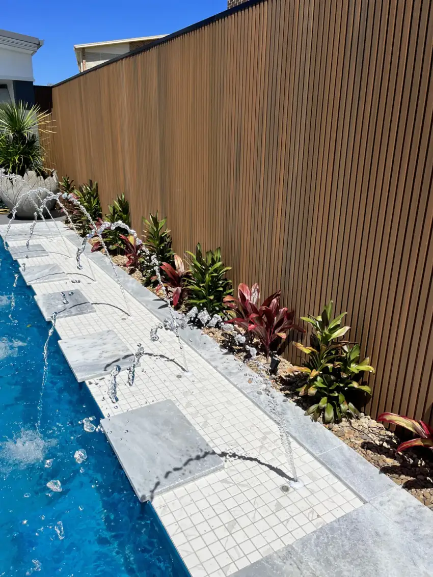 A tiled water feature spilling into a pool against a timber-batten screen with native planting.