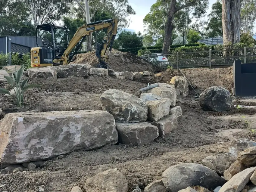 A large sandstone boulder retaining wall built across a steep, cleared block.