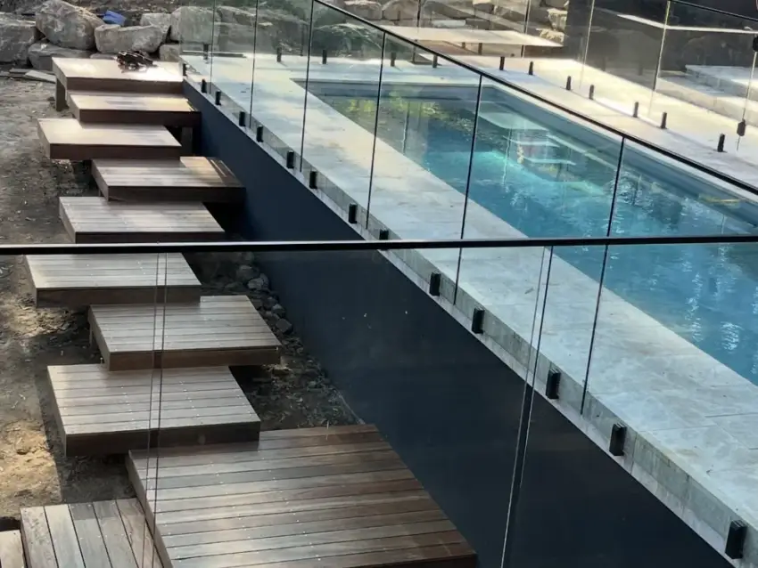 Cantilevered timber steps and frameless glass fencing running beside a lap pool.
