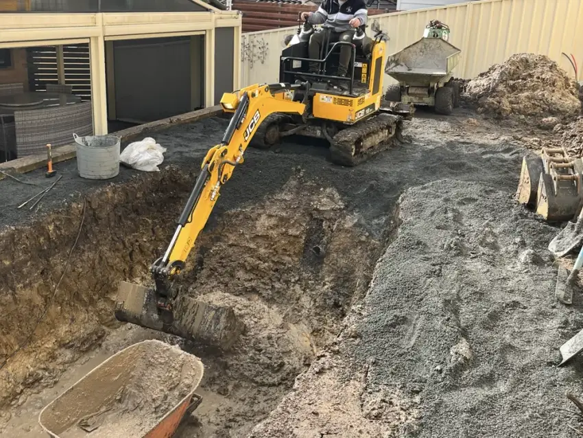 An excavator digging out a new pool and retaining on a suburban site.